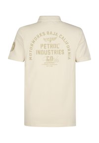 Kermanvärinen poolopaita, jossa on kauluksellinen pääntie ja beigen värisiä tekstuurilla varustettuja logopainatuksia sekä grafiikoita selässä ja vasemmassa hihassa.