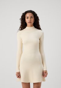 Abito a maniche lunghe in maglia color crema con vestibilità dritta e trama a coste, dotato di un collo alto e gonna svasata.