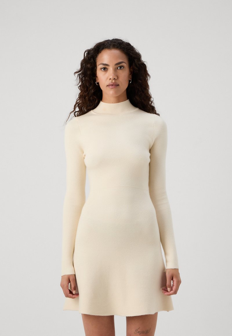 Abito a maniche lunghe in maglia color crema con vestibilità dritta e trama a coste, dotato di un collo alto e gonna svasata.