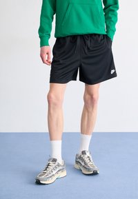 Black athletic shorts with a drawstring waist, paired with gray and beige running shoes featuring mesh details and a prominent Nike logo.