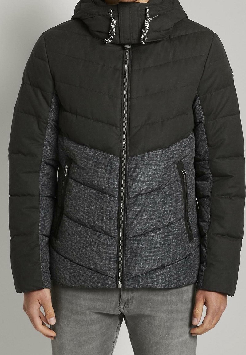 Padded jacket z czarną górną częścią i teksturowaną szaro-dolną częścią. Posiada zamek błyskawiczny, kaptur ze sznurkami oraz kieszenie na zamek.