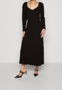 Svart, långärmad midiklänning med texturerat tyg och V-ringning. Kombinerad med svarta spetsiga klackar med dekorativ hårdvara.