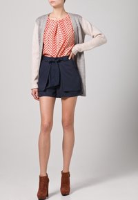 Cardigan grigio chiaro su una blusa a zigzag rossa e bianca, abbinato a pantaloni corti navy su misura e stivali ankle in suede marrone.