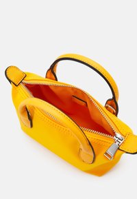 Sac à main jaune avec double poignée et fermeture éclair argentée ouverte, dévoilant une doublure intérieure orange et une petite poche intérieure.