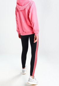 Rosa huppartröja med texturerad rygg, kombinerad med svarta leggings med rosa sidostripes. Vita sneakers fulländar looken.