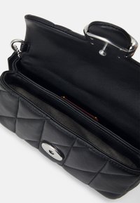 Sac à main en cuir noir matelassé ouvert, montrant les compartiments intérieurs et la fermeture à fermoir argenté.