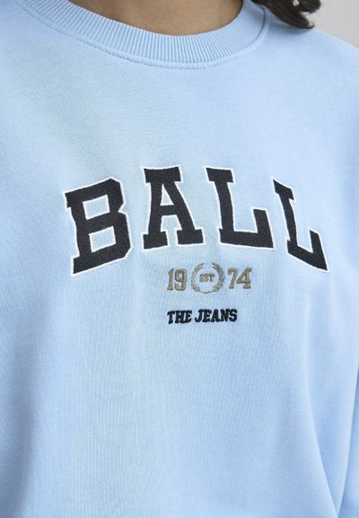 Lyseblå hettegenser med ribbet halslinning. Har "BALL" i svart broderi, "1974" i gull, og "THE JEANS" i svart tekst under.