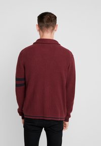Maglione bordeaux in maglia con colletto, caratterizzato da righe nere sulle maniche, tessuto testurizzato e vestibilità morbida.