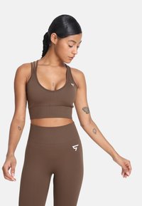 Brązowy sportowy crop top z cienkimi ramiączkami, okrągłym dekoltem i wspierającym pasem. Pasujące legginsy o wysokim stanie, obie wykonane z elastycznego materiału.