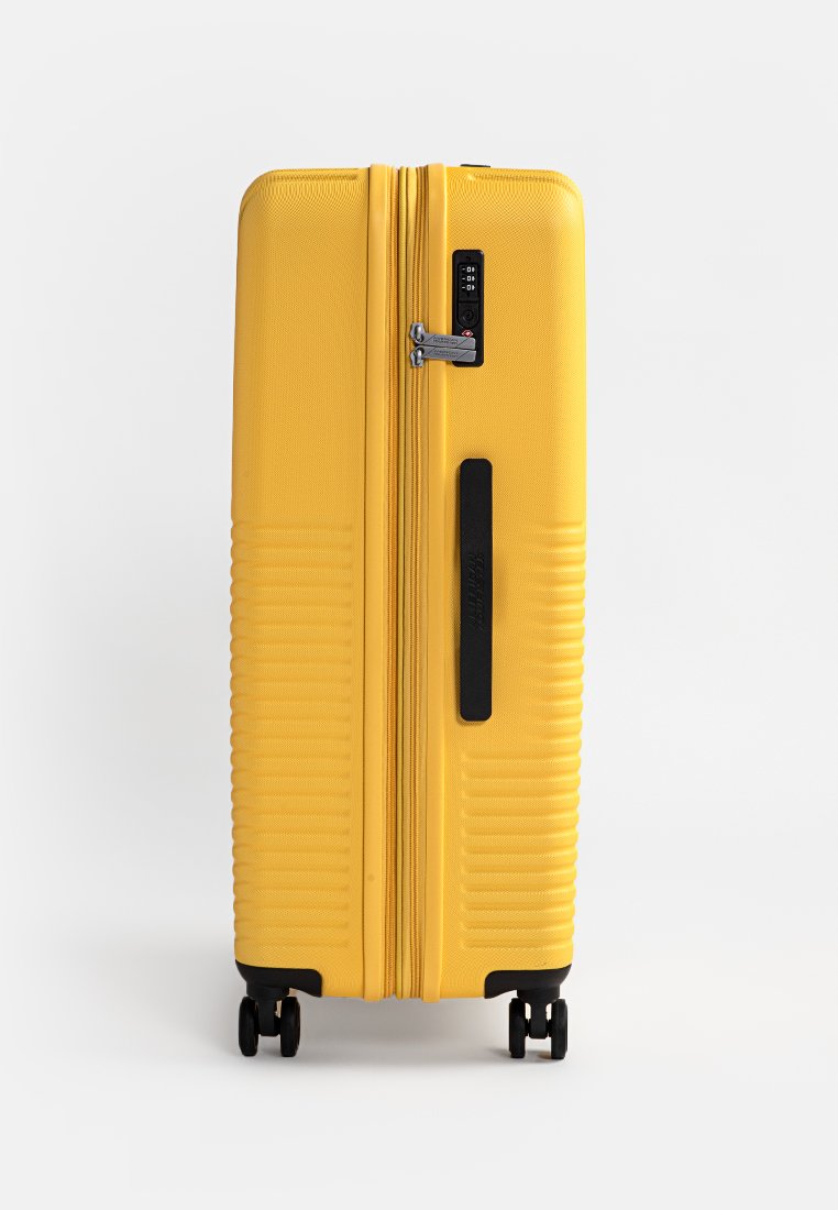Valigia rigida gialla con superficie textured, doppie cerniere, lucchetto a combinazione e quattro ruote nere per una migliore mobilità.