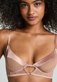 Lace en satijnen beha in zachtroze met een triangle cupvorm, voorzien van een keyhole-detail en verstelbare bandjes. Soepele textuur en delicate accenten.