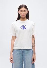 Λευκό βαμβακερό T-shirt με στρογγυλή λαιμόκοψη, κοντά μανίκια, με μπλε λογότυπο "K" και κείμενο "Calvin Klein" στο μπροστινό μέρος. Σχεδίαση με χαλαρή εφαρμογή.