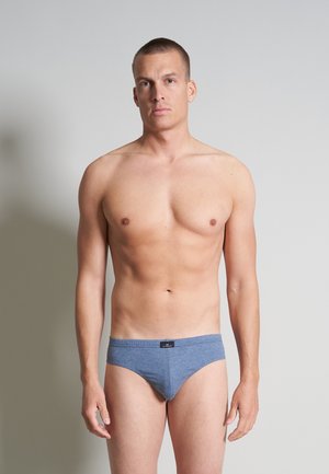 Blauwe katoenen slipjes met een zachte textuur, voorzien van een zwart logo-label op de tailleband. Het model toont een neutrale pose.