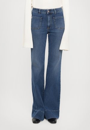 Flared jeans in dark blue denim, featuring a high waist, five pockets, and contrasting stitching. The bottom hem is wide with a cuffed finish.