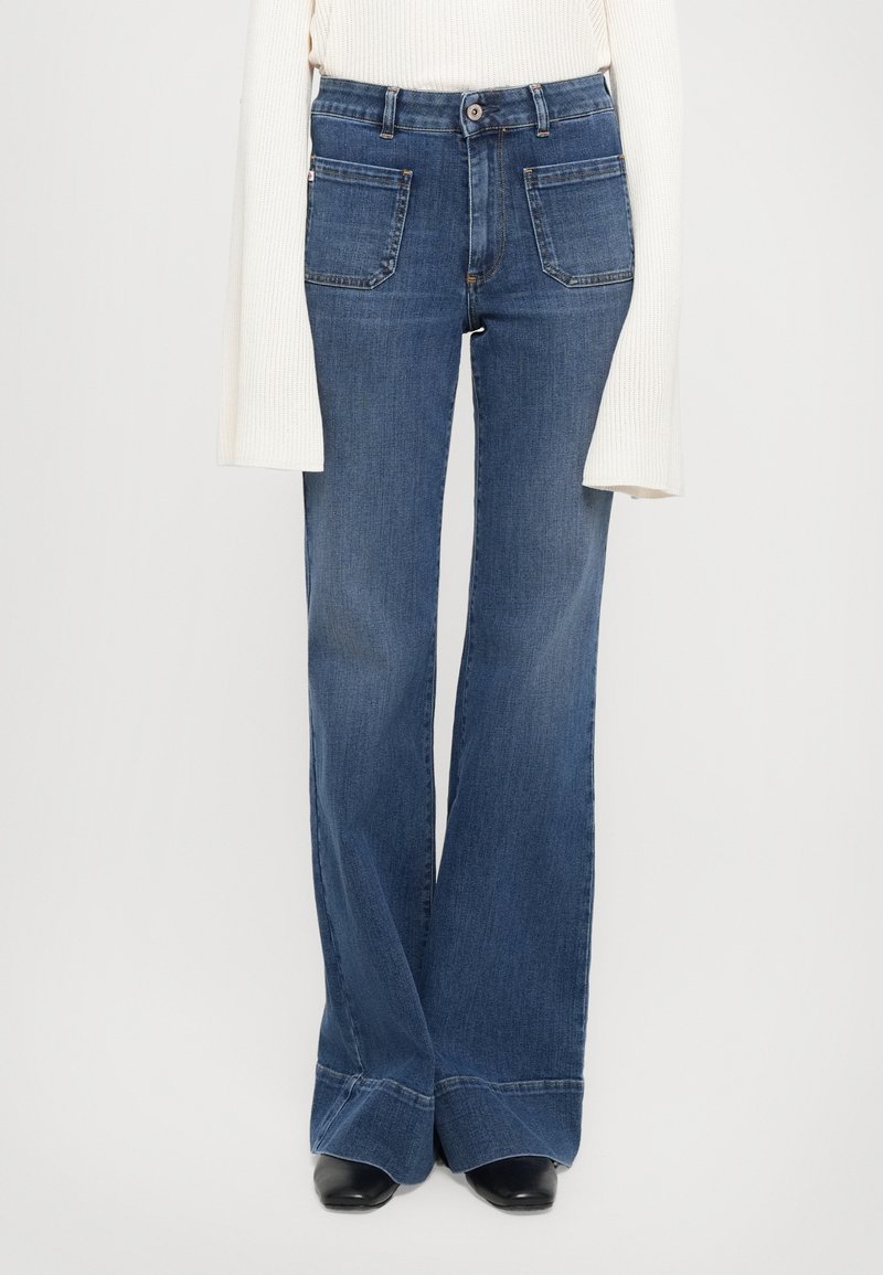 Jeans a zampa d'elefante in denim blu scuro, con vita alta, cinque tasche e cuciture a contrasto. L'orlo inferiore è ampio con una finitura arrotolata.