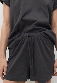 Tamno sivi pamukasti šorc s opuštenim krojem, elastičnim pojasom i uzicom. Materijal je mekan bez vidljivih uzoraka ili hardvera.