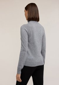 Grauer Strickpullover mit hohem Kragen, langen Ärmeln, gerippten Bündchen und Saum. Mit strukturierten Akzenten entlang der Schultern.