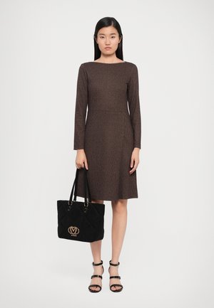 Brown textured dress with long sleeves and a round neckline, paired with a black quilted handbag and strappy black sandals.