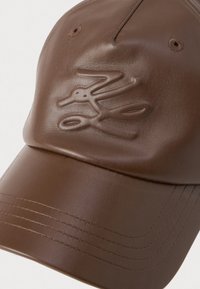 Gorra de cuero marrón con un diseño cosido, que presenta un logotipo en relieve. Textura suave y visera curva con agujeros de ventilación.