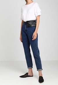 Camicia bianca a volant con maniche corte, jeans blu a vita alta, borsa a cintura in pelle nera, scarpe in tela nere senza lacci, jeans risvoltati alle caviglie.