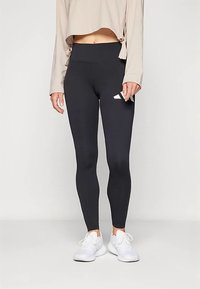 Leggings nere a vita alta, realizzate in tessuto liscio ed elastico. Presentano un piccolo logo bianco sul lato sinistro, abbinate a sneakers bianche.