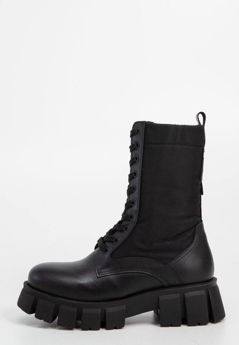 Botas de tobillo negras que combinan cuero y tela, con puntera redonda, suela gruesa y cordones en la parte delantera con ojetes de metal.