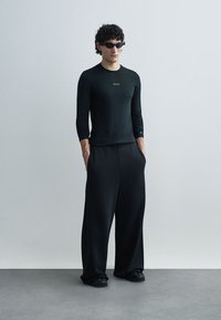 Zwarte shirt met lange mouwen, losse zwarte broek en donkere zonnebril. Gladde stoffen, minimalistisch ontwerp en geen zichtbare patronen.