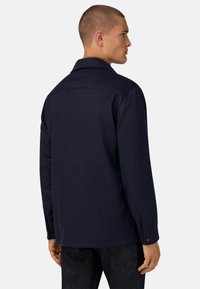 Marinblå lättviktsjacka med krage, långa ärmar, knappade cuffs och rak skärning. Slät textur, minimalistisk stil.