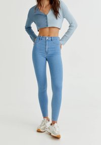 Vaqueros ajustados de cintura alta en azul claro, con una textura suave, diseño ceñido y sutilezas en las costuras, combinados con un top corto de canalé.