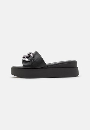 Sort platformsandal med en kraftig kædedetalje. Glat læderoverdel, bred rem og en tyk, tekstureret sål for stabilitet.