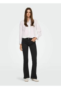 Camisa blanca de botones, pantalones vaqueros negros acampanados y zapatillas blancas. El atuendo presenta cortes clásicos y una silueta ajustada. Texturas suaves en todo.