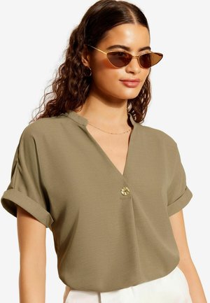 Blusa khaki a maniche corte con scollo a V e risvolti, dotata di un bottone decorativo all'escollatura. Tessuto dalla consistenza liscia.