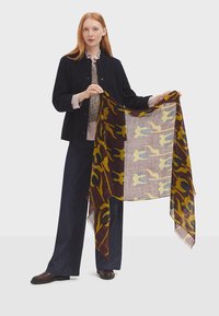 Multi-colored scarf featuring a floral pattern in yellow and blue on a burgundy background. Lightweight, textured fabric edges are fringed.