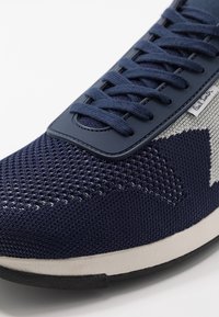 Baskets en maille bleu marine et blanc avec bout texturé, lacets assortis et petite étiquette en tissu sur le côté portant la mention « Paul Smith ».
