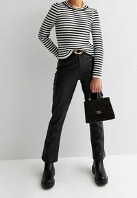 Pull rayé noir et blanc à col rond, associé à un pantalon en simili cuir noir. Accessoirisé avec un petit sac à main noir texturé.