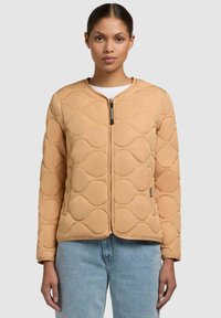 Giacca trapuntata beige con collo rotondo, cerniera frontale e dettagli a motivo ondulato. Presenta maniche lunghe e una silhouette aderente.