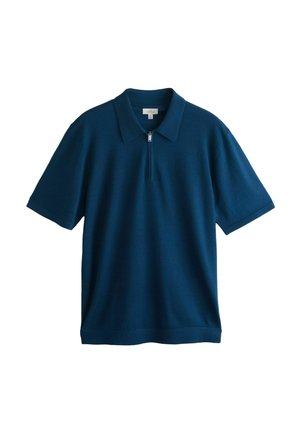 Szakállas férfi, só-bors arcszőrzettel, sötétkék kötött pulóvert visel, melynek cipzára részben felhúzva a gallérján.