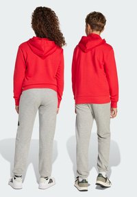 Un sweat à capuche rouge associé à un pantalon de survêtement gris. Le sweat a un ourlet et des poignets côtelés, tandis que le pantalon dispose d'une taille élastique.