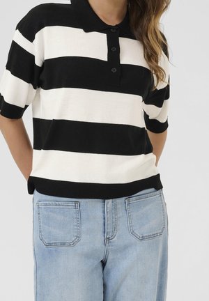 Czarna i biała krótkim rękawem polo w paski z kołnierzykiem, czarnymi guzikami i prążkowanym dołem, w zestawieniu z jasnoniebieskimi dżinsami.