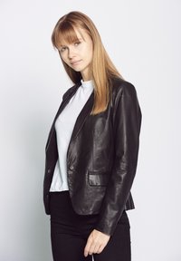 Schwarze Leder-Blazer mit sleekem Design, ausgestattet mit einem Reverskragen, zwei Fronttaschen und glatter Textur; getragen über einem weißen Hemd.
