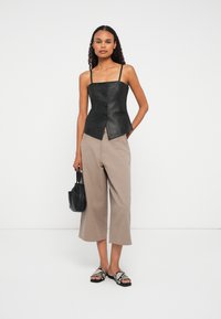 Naisterahvas, kes kannab musta nahkse nööpidega korsetti, beeže laiad lõikega lühikesed püksid, madu nahast sussid ja hoiab käes väikest musta käekotti.