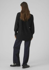 Maglione nero lavorato a maglia con un motivo a diamante testurizzato, abbinato a jeans blu scuro a gamba larga e mocassini neri.