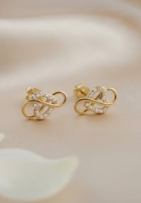 Guldpläterade örhängen med en sammanflätad design, prydda med små klara stenar och med en polerad, slät yta.