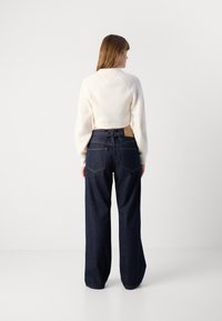 Cream ribbed sweater with long sleeves, cropped length, paired with high-waisted dark blue wide-leg jeans featuring a rear belt detail.