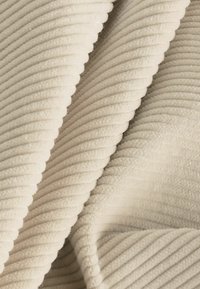 Textured cream-colored fabric with soft, ribbed lines, featuring a plush, velvety appearance and subtle sheen. Ideal for upholstery or garments.