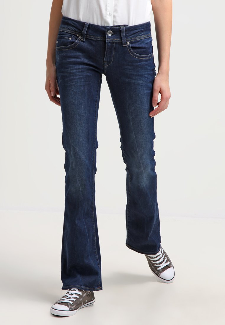 Dark blue flared jeans with a classic five-pocket design, light fading, and a button closure. Worn with gray low-top sneakers.