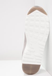 Nike-sneakersula med en vit gummibas med texturerat mönster, grå mockaövre och en slät brun hälaccent.