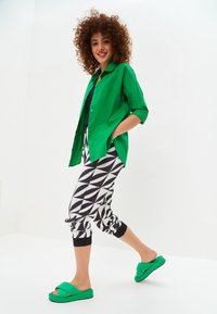 Groene oversized shirt, zwarte tanktop, gestreepte zwart-wit tapse broek en groene platform sandalen. Zachte stof, relaxte fit.
