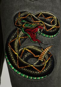 Serpent brodé enroulé avec une bouche ouverte rouge, une langue verte, des marques jaunes et orange sur un fond de tissu gris foncé.