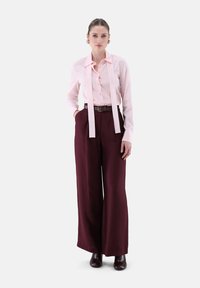 Light pink blouse with long ties, paired with high-waisted burgundy wide-leg trousers. Smooth textures with a structured design.